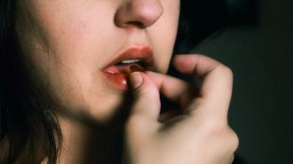 Closeup of a woman placing a pill in her mouth.