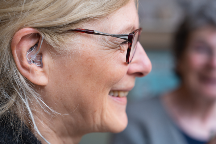 a close up on the side of a woman's face. in her ear is a small device