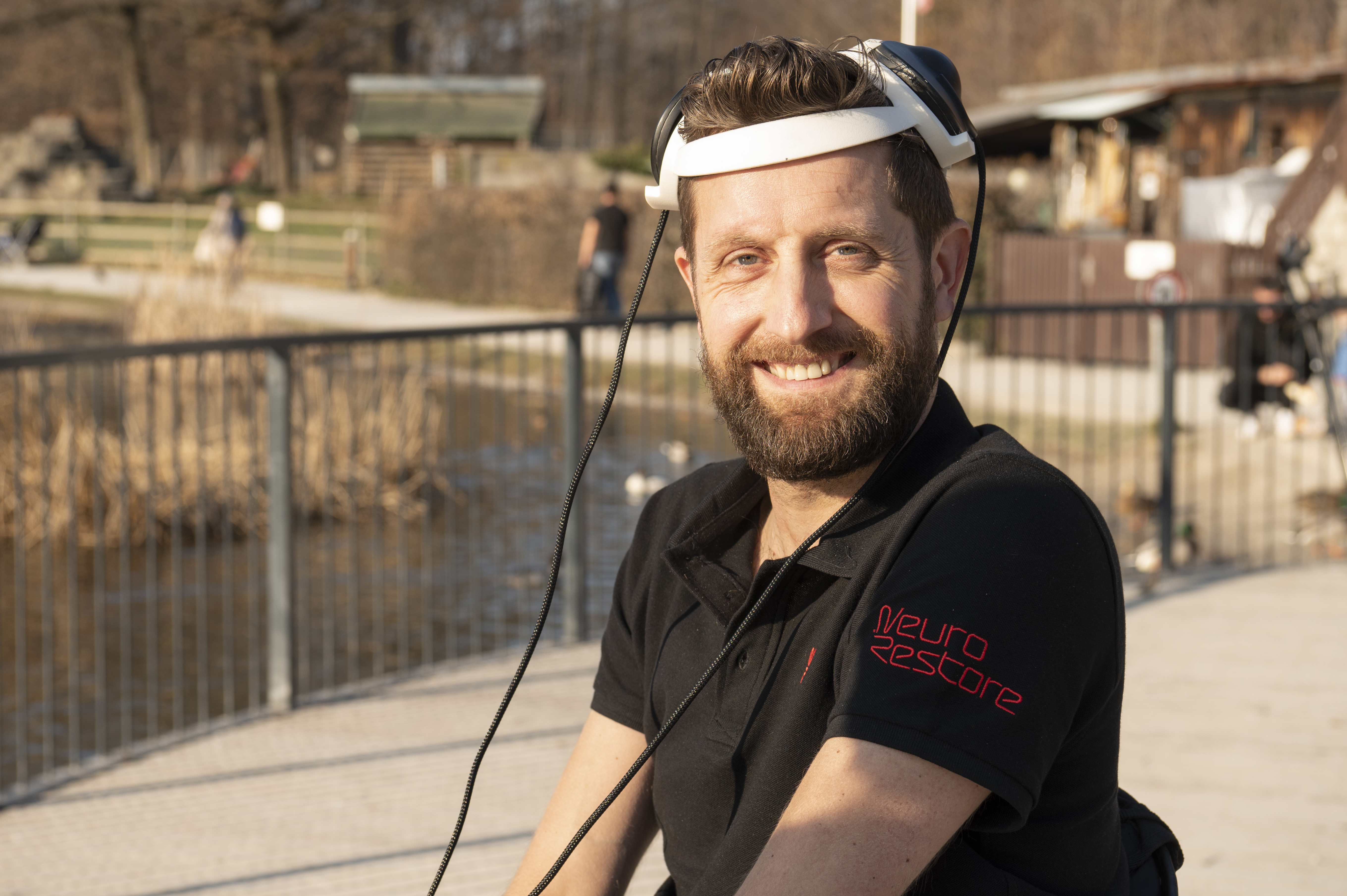 a man wearing a helmet with two wires extending from it. He is outside on a foot bridge.