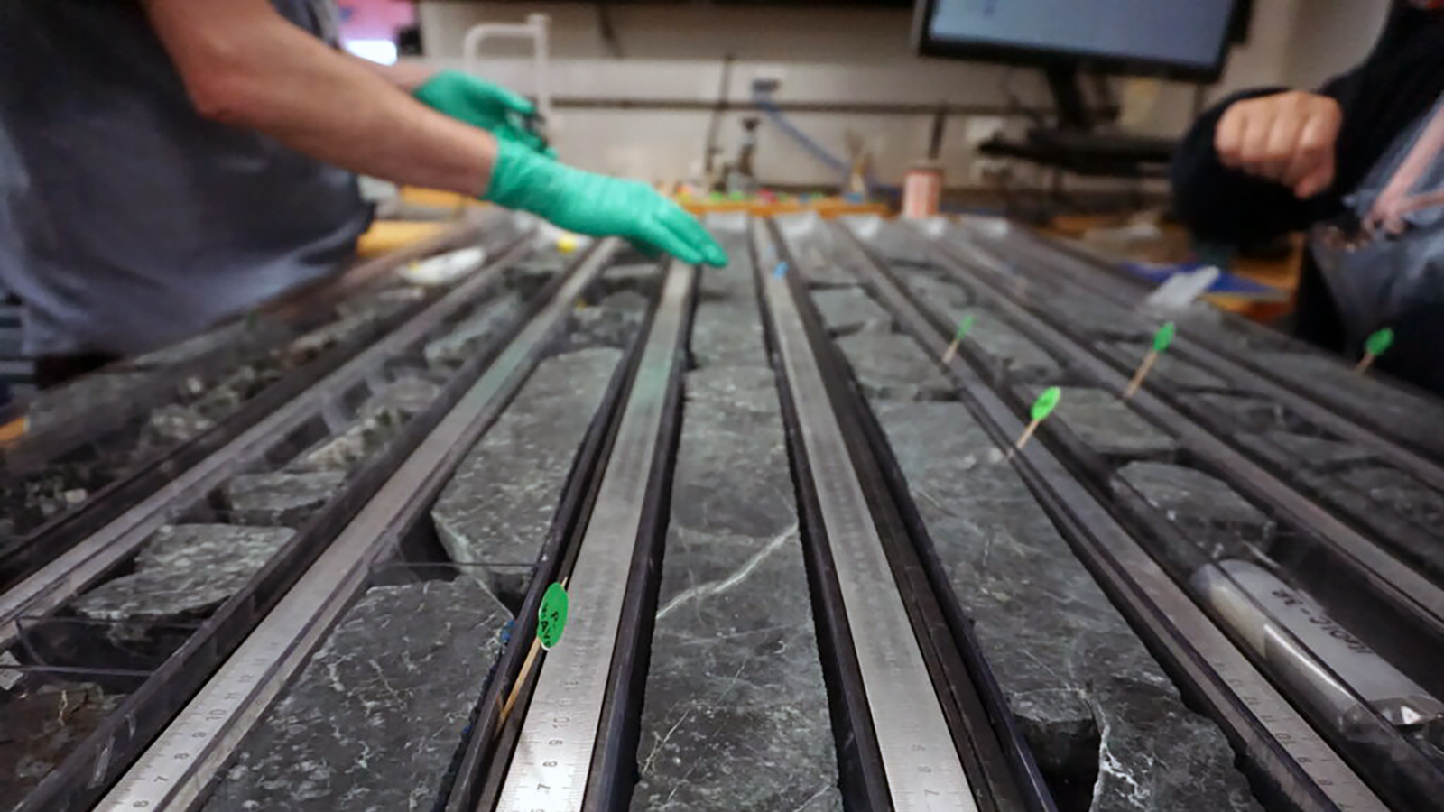 rows of black rock with the gloved hands of a scientist in the background