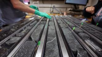 rows of black rock with the gloved hands of a scientist in the background